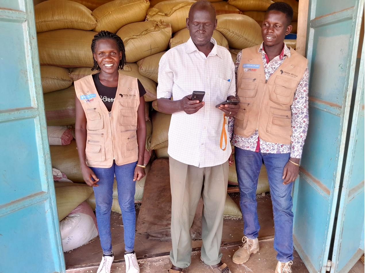 Field staff in branded vests interviewing a trader inside an agricultural produce store