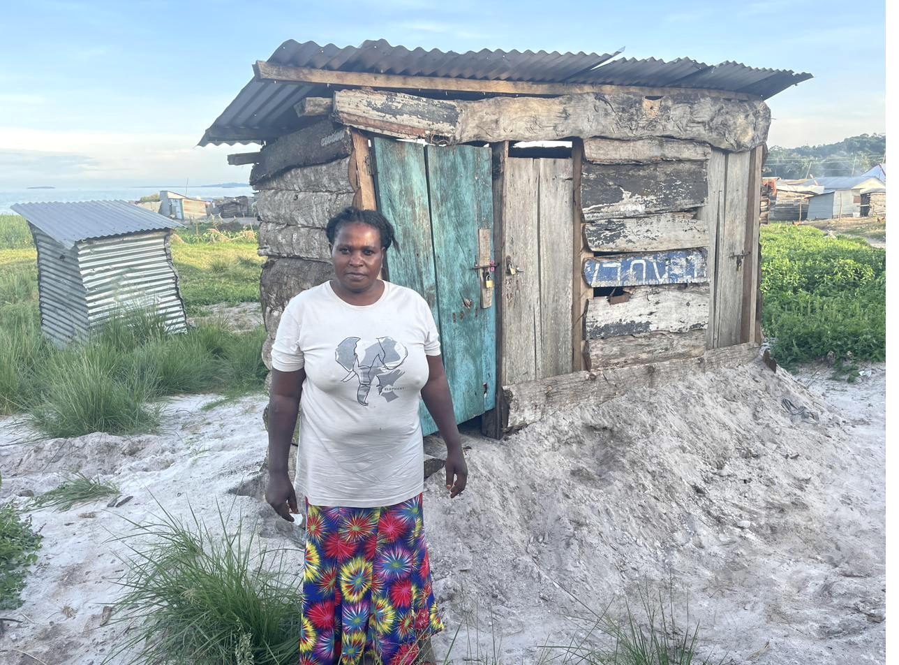 A woman standing outside a small structure at a lakeside landing site in Kalangala during household data collection